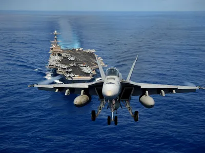 An F/A-18E Super Hornet from the Tophatters of Strike Fighter Squadron (VFA) 14 flies past aircraft carrier USS John C. Stennis in April 2013.