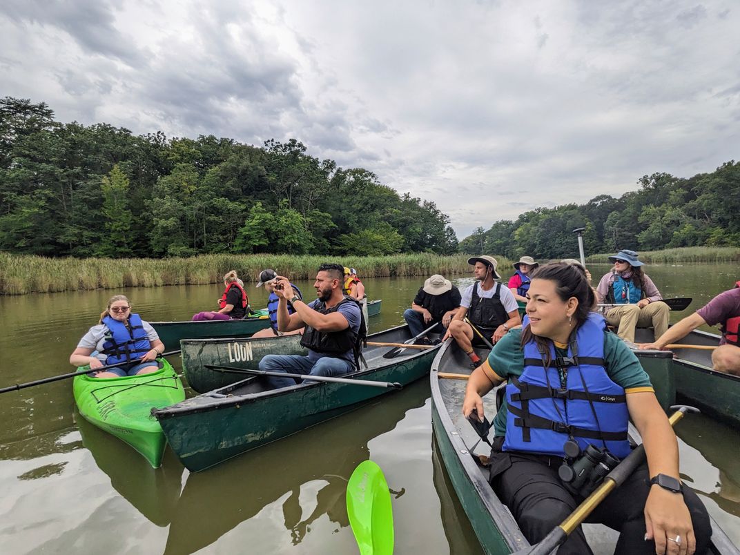 A group of people are in several canoes on a river, observing nature and taking pictures