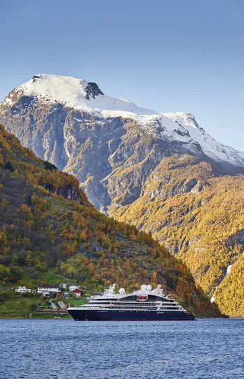 Small-Ship Ocean Cruises - A small cruise ship floating in front of a snow-capped mountain lit by sunlight.
