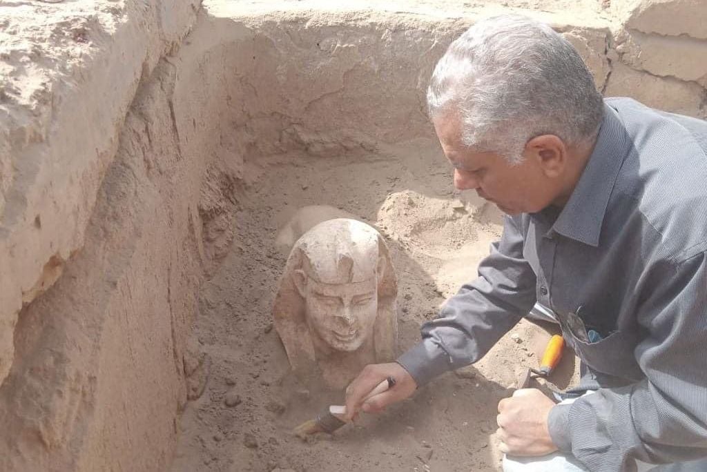 Researcher using a brush to dust off a statue of a sphinx