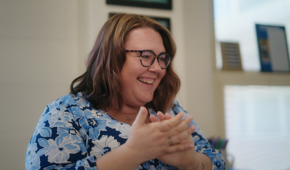 Teacher with short brown hair and glasses, wearing a blue shirt is smiling and clapping