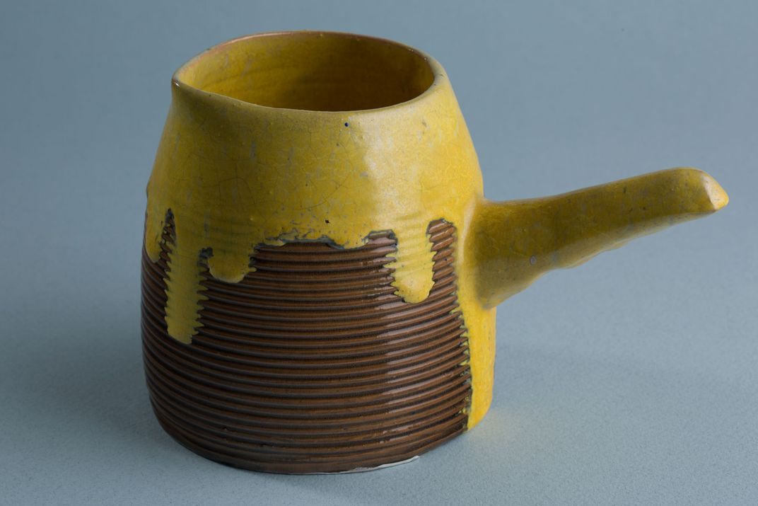 A ceramic pot glazed at the top with a bright yellow glaze, dripping down its sides. The bottom of the pot is glazed in a warm brown and has a ribbed texture.