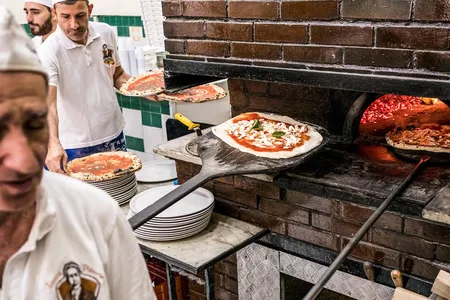 The main oven at Pizzeria Da Michele is near customers’ tables. The waiter in the background holds marinaras.