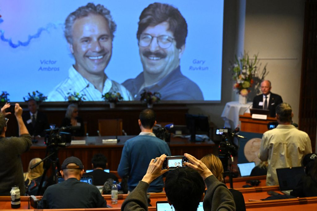 a journalist takes a picture with a phone of the two Nobel winners projected on a screen in a lecture hall