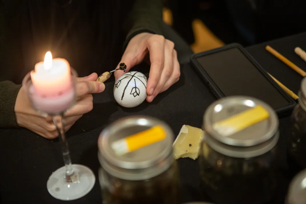 An individual melts hot wax onto an egg in a floral design