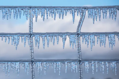 Icicles form on a fence and reflect the blue sky after an ice storm.