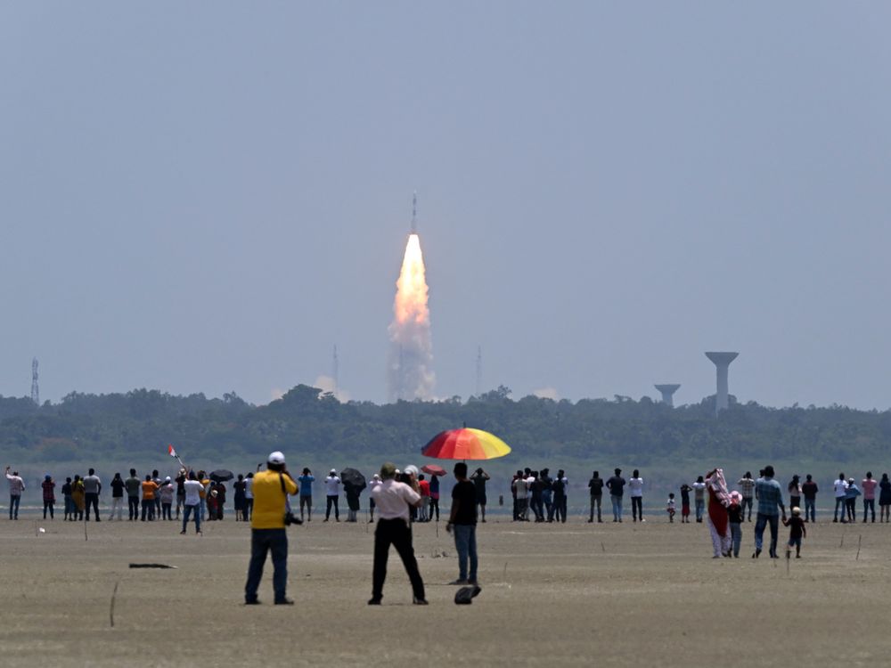 People stand and watch as a rocket takes off in the background