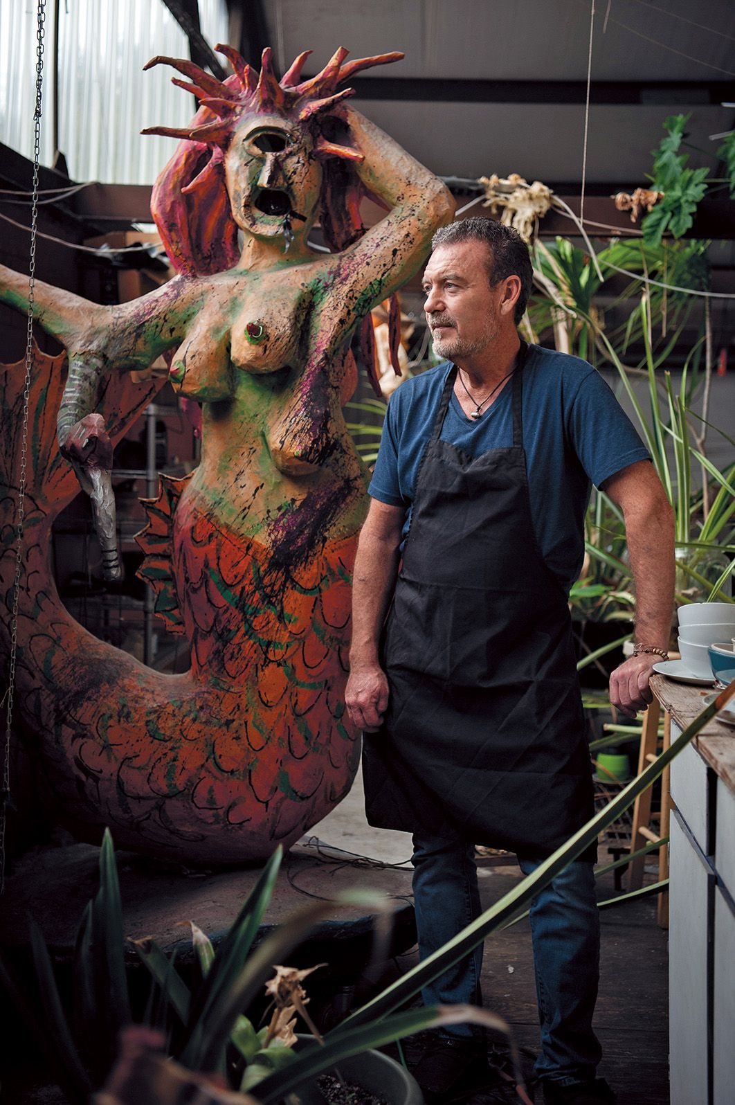 a man stands next to a wooden mermaid for a portait