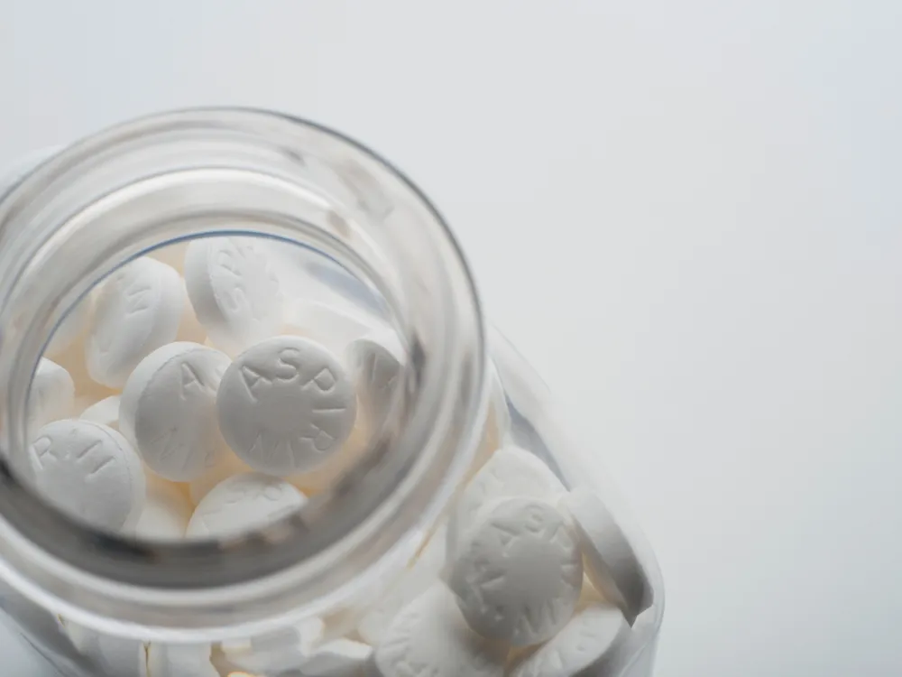 An image of a glass bottle filled with white tablets of aspirin. The bottle is shown from the top and is against a white background.