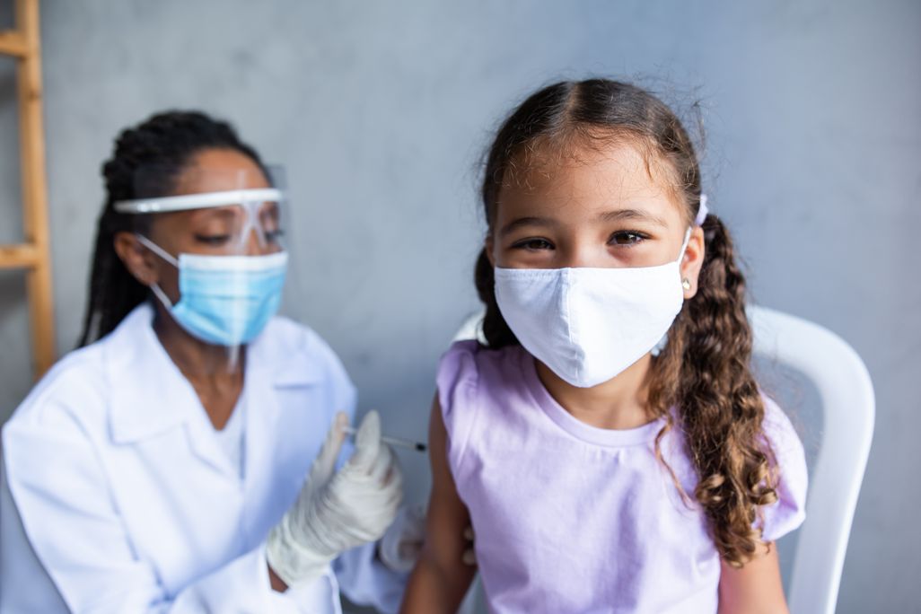 An elementary school aged girl wearing a face mask gets a vaccine