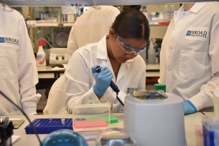 A young girl wears a lab coat, safety goggles and blue latex gloves in a research laboratory