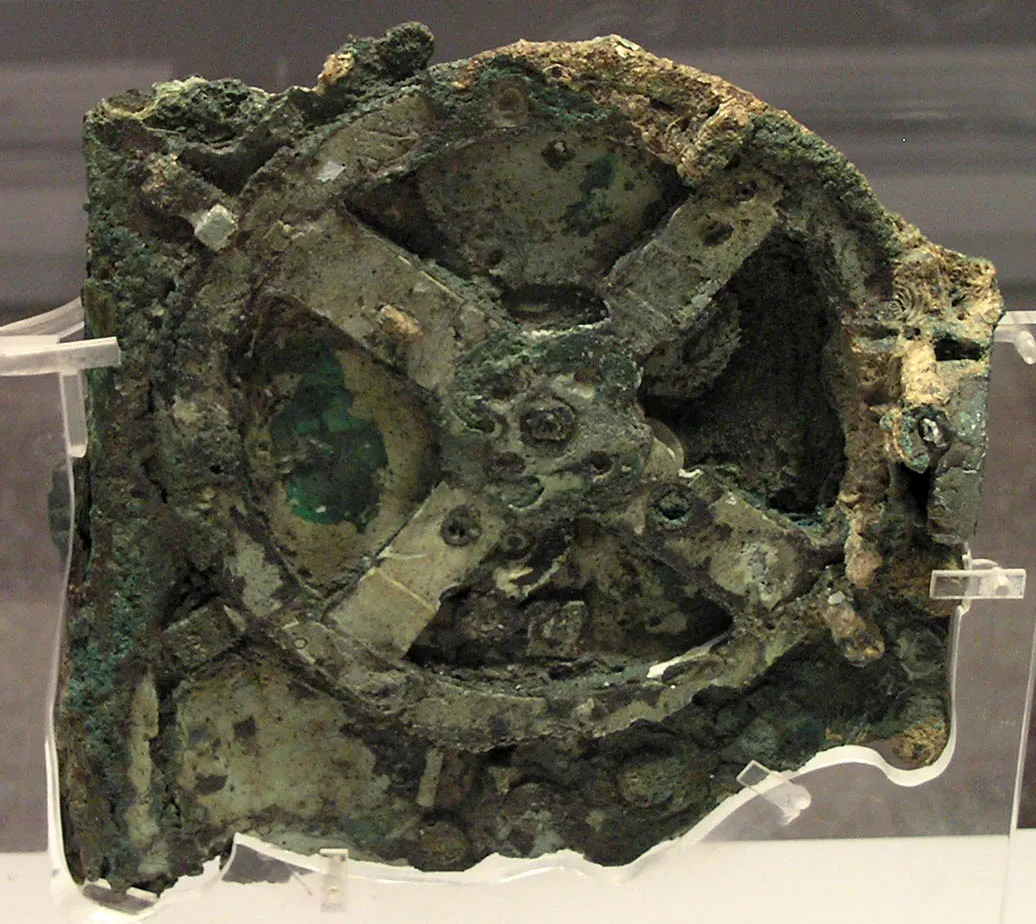 A rusted, green, degraded gear in the shape of an X with a circle around it, on display in a museum