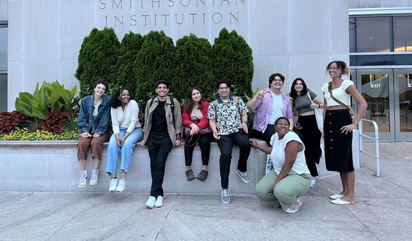 A group of student interns gather in front of a grey building
