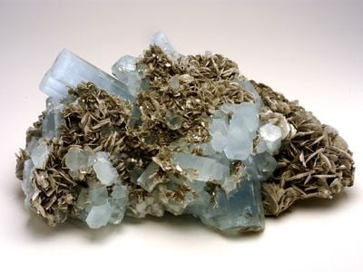 A chuck of natural, light blue and gray aquamarine beryl on white background.