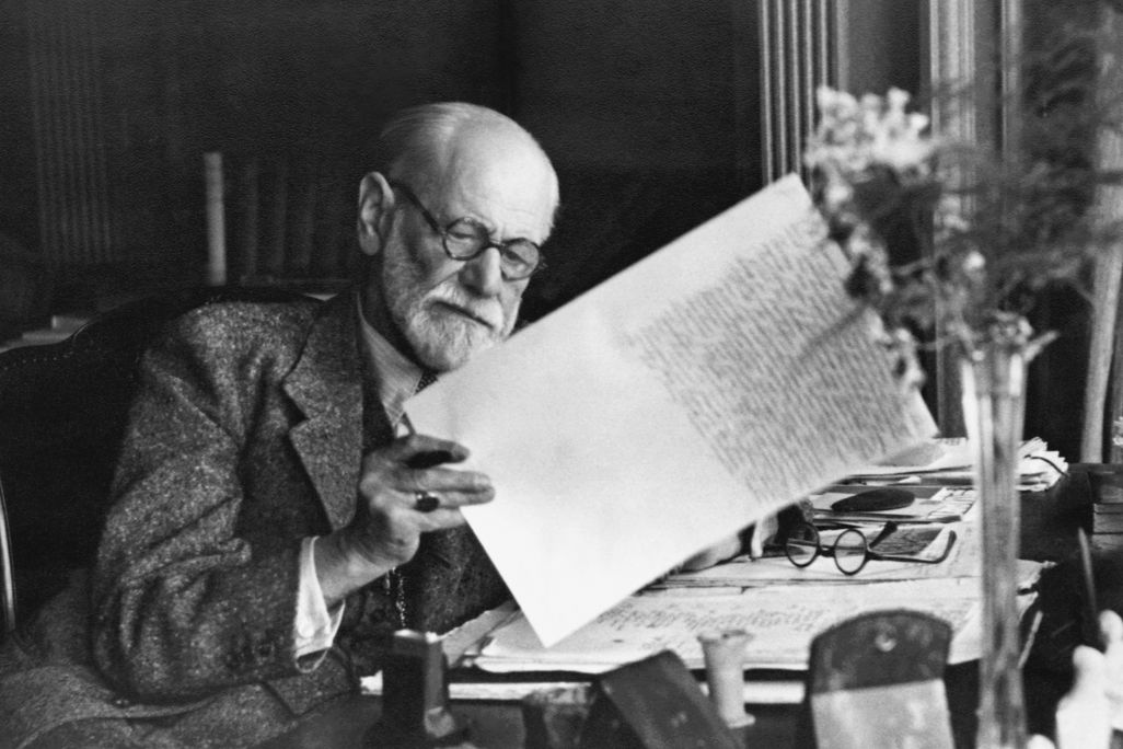 Old man with glasses looking at a piece of paper while sitting at a desk