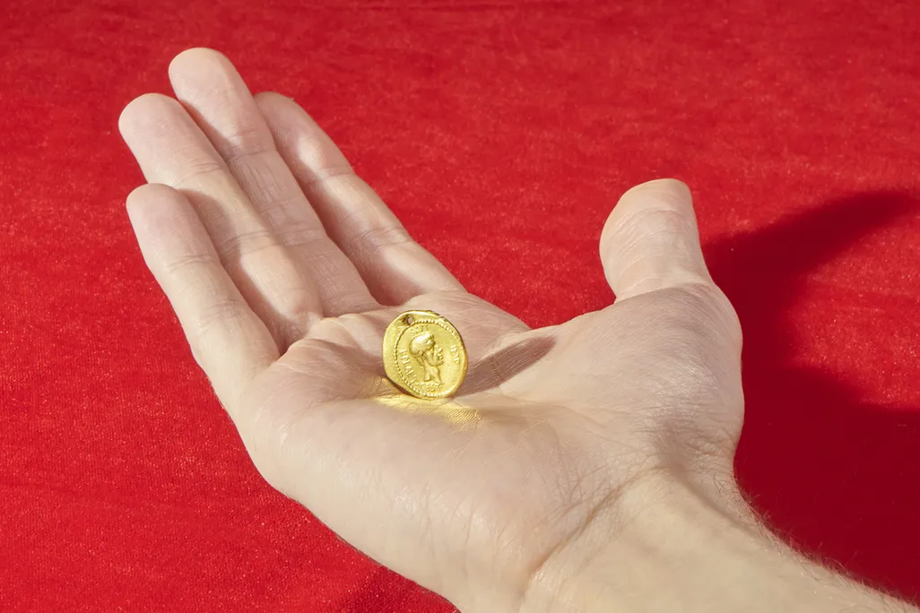 A white hand extends over a red background and holds the golden coin in their palm