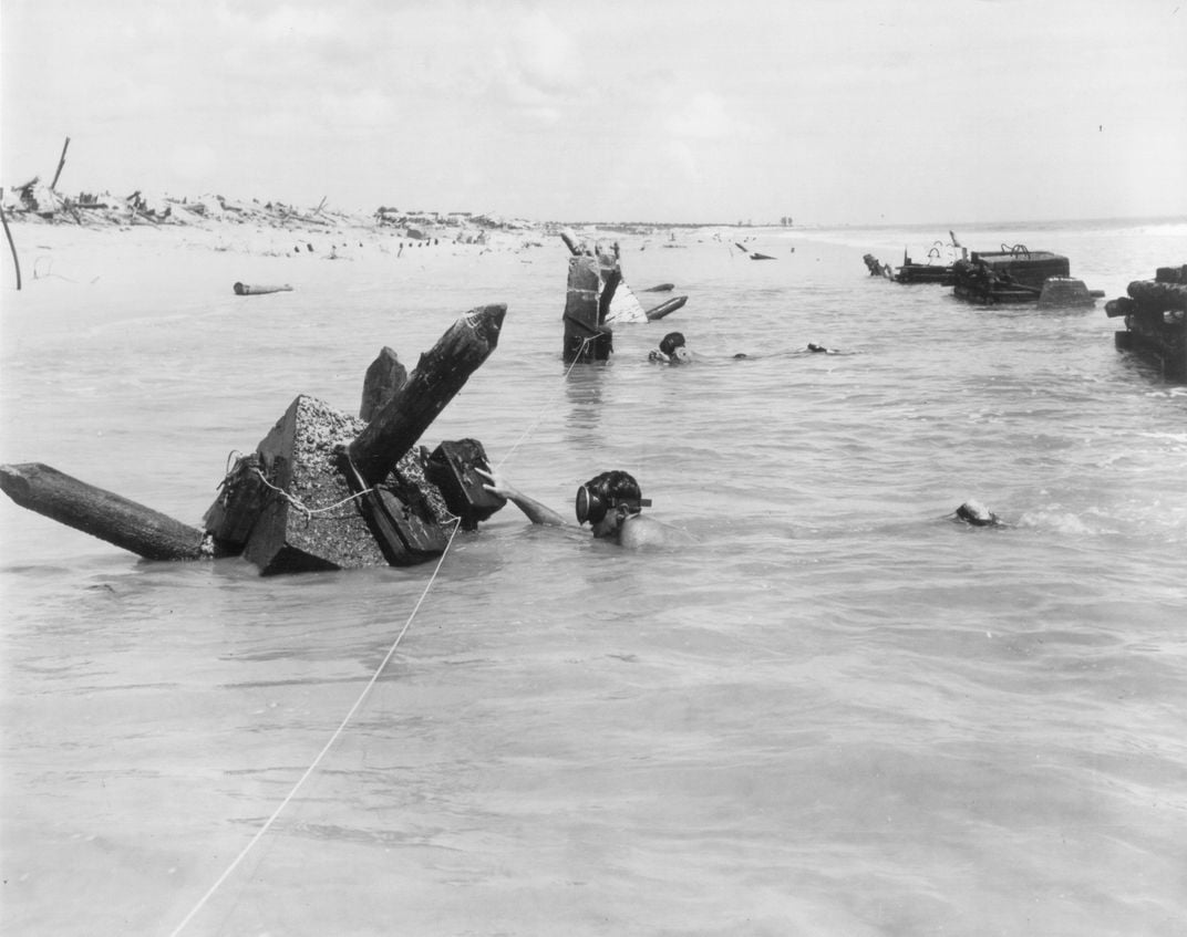 UDT men swimming in stealth toward a row of beach obstacles