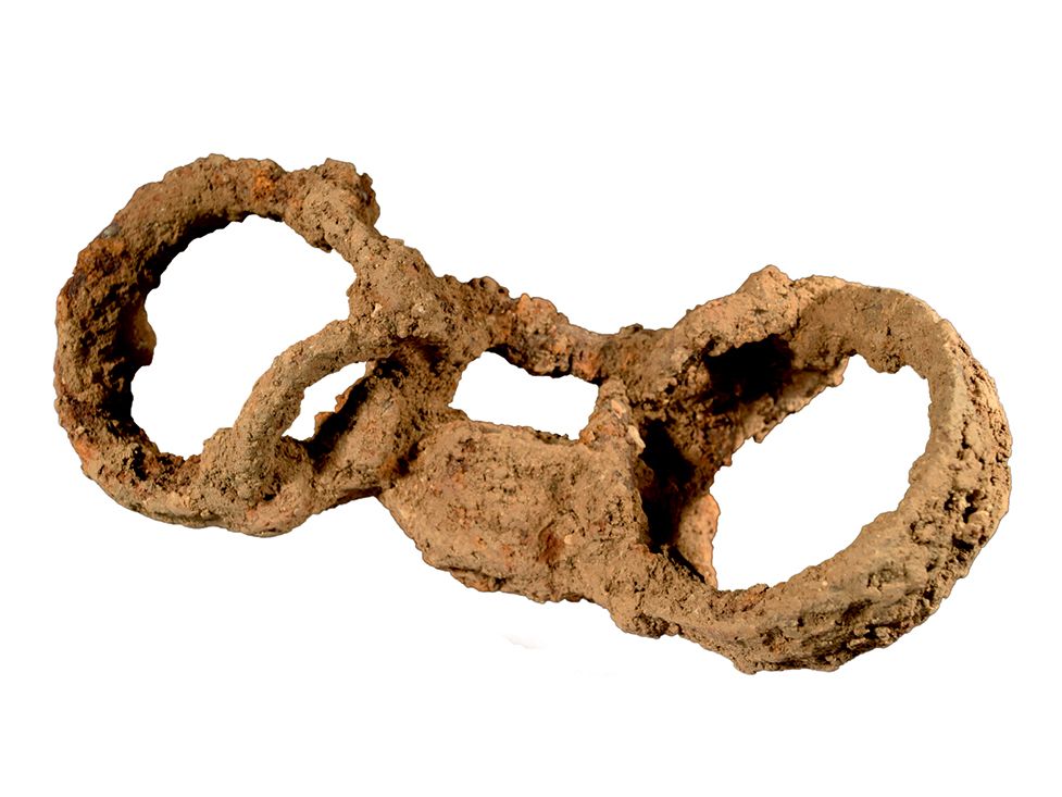 An image of a very rusted pair of shackles, two circles connected by a padlock that would have encircled someone's ankles