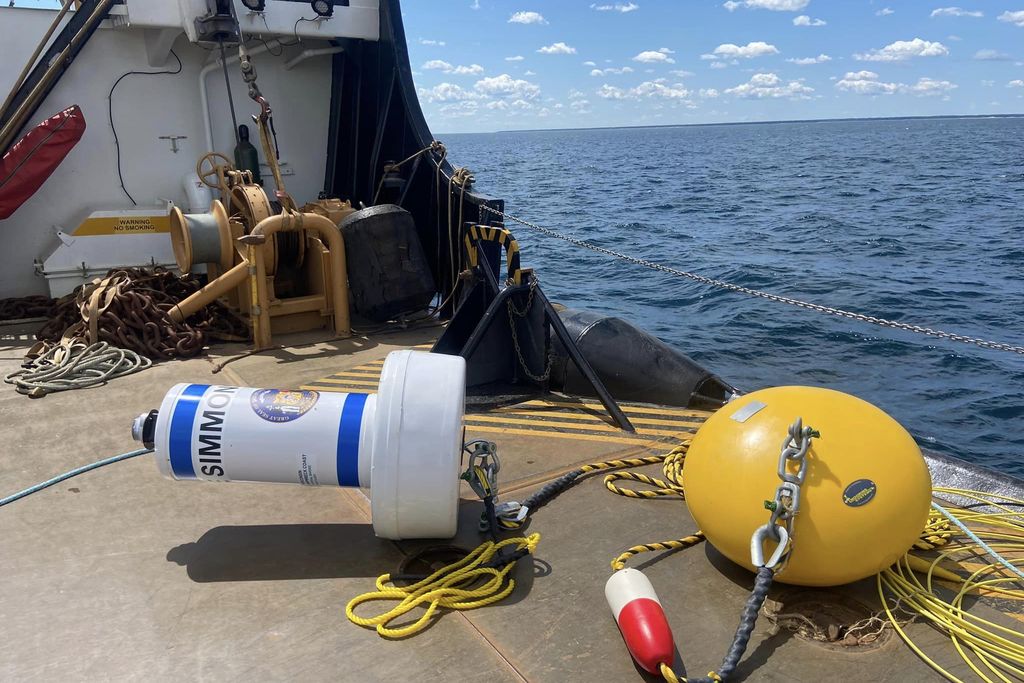 A white buoy attached to a yellow circular-shaped object next to water