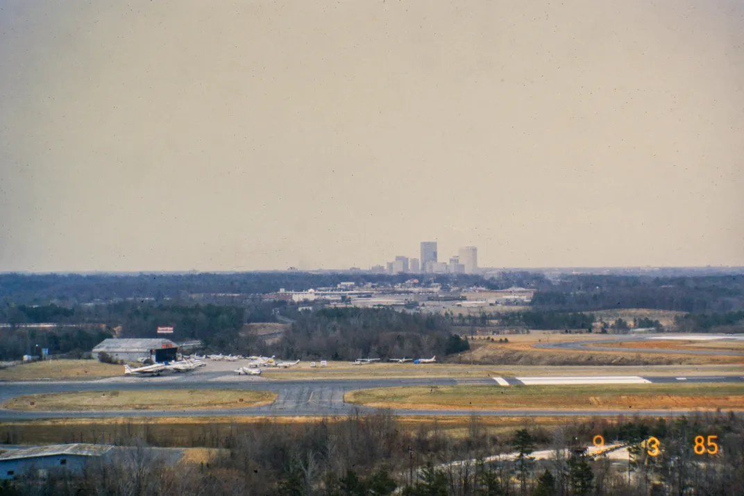A view of a runway and hangar with a city skyline in the far background.