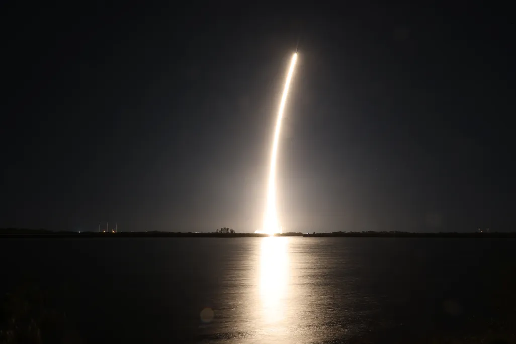 a rocket launch shows a golden streak over the water in the dark