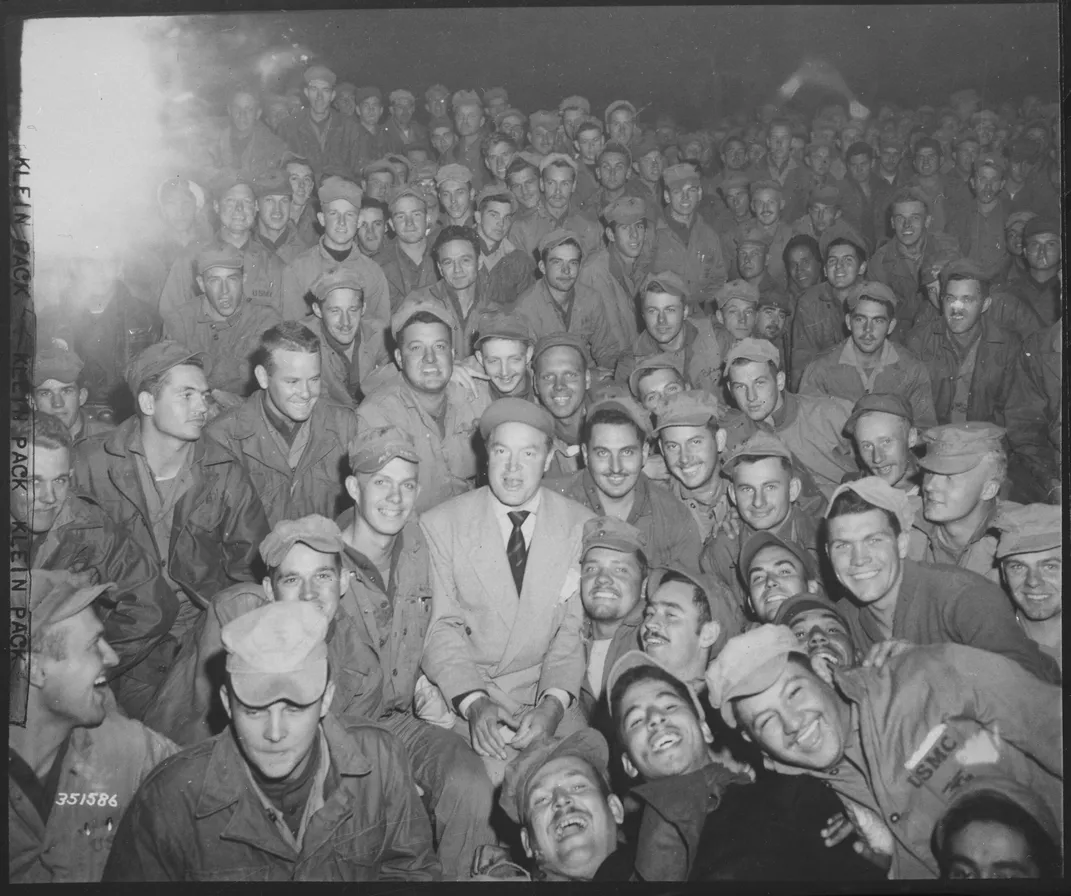 Bob Hope (center, in suit) sits with American service members in Korea in 1950.