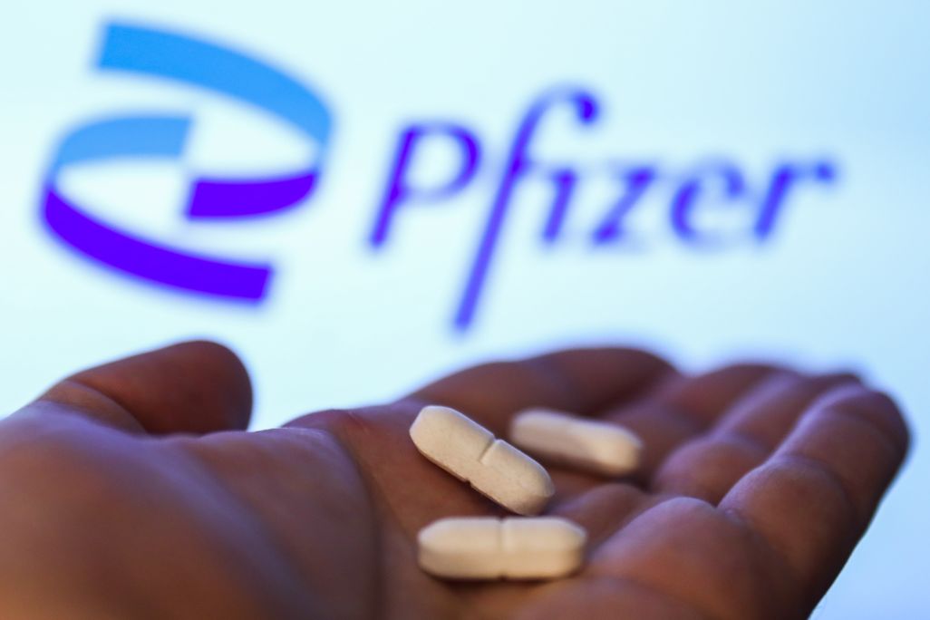 Hand holding three while tablet pills against Pfizer branded backdrop