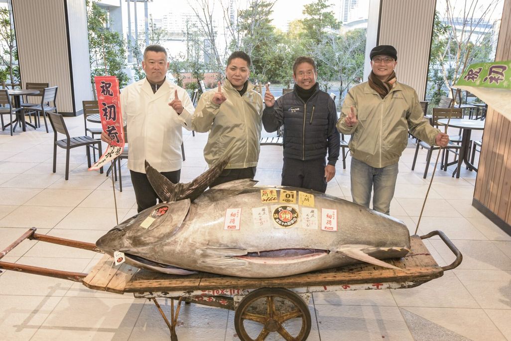 A giant fish on a rolling cart with four people standing behind it holding up their index finger in a No. 1 sign