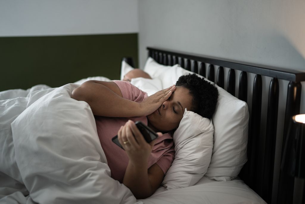 A woman lays in bed and looks at her phone