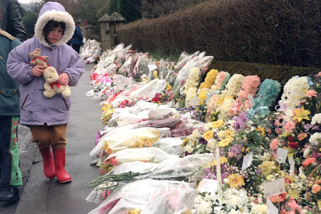 A young girl walks past a row of flowers honoring her murdered classmates and teacher