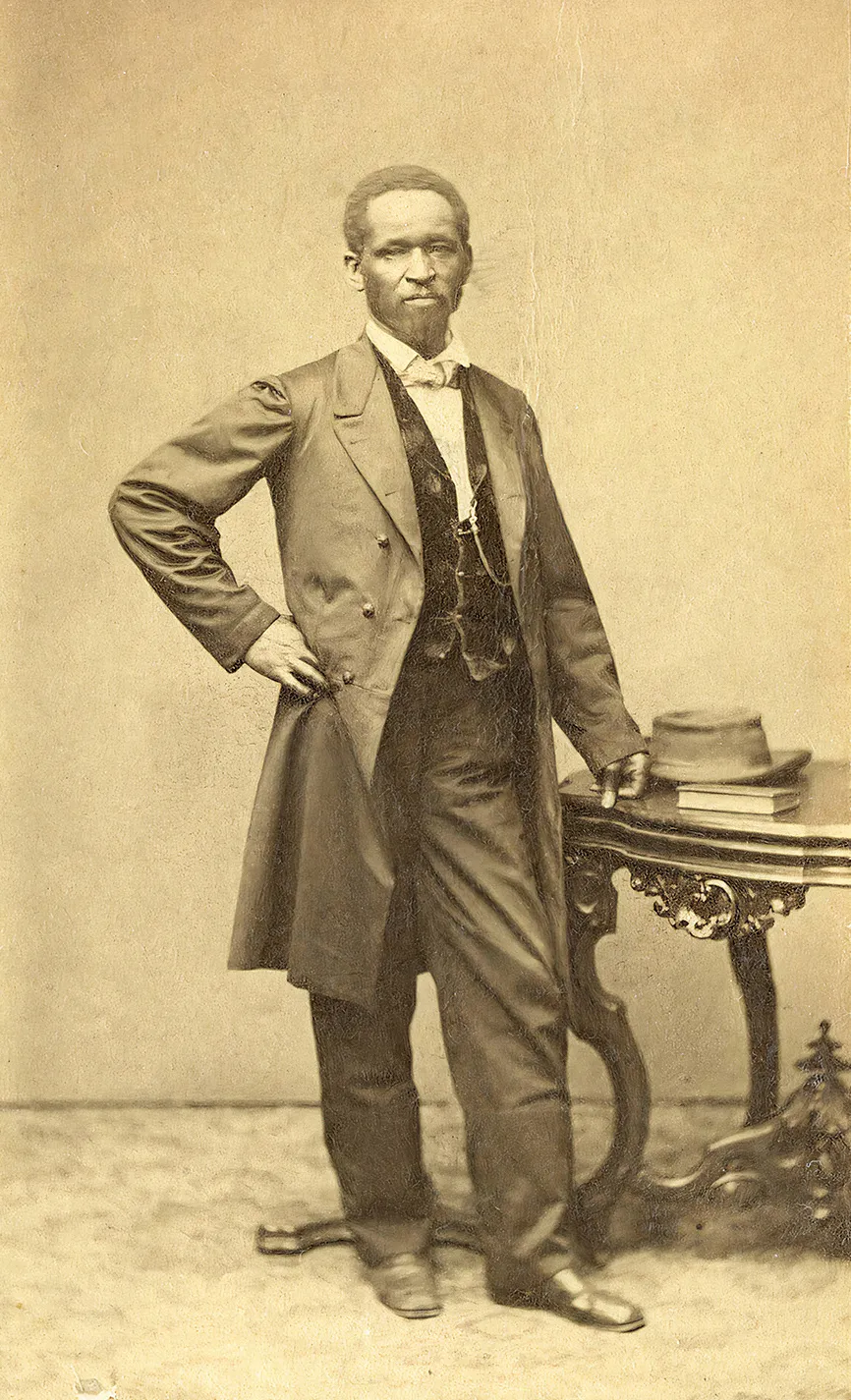 a man in a suit standing next to a table poses for a portait
