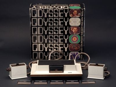 The Magnavox Odyssey system arrayed in front of its cover box. The box is decorated with the system's name and small images of various games and children using the Odyssey's controller