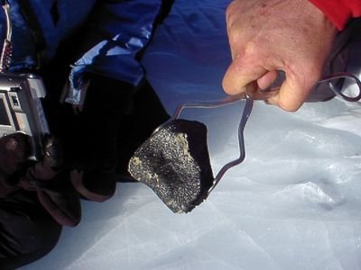 A meteorite in the process of being recovered by volunteers in the Antarctic Search for Meteorites program. The shiny fusion crust on this meteorite suggests it may be an achondrite. (ANSMET)