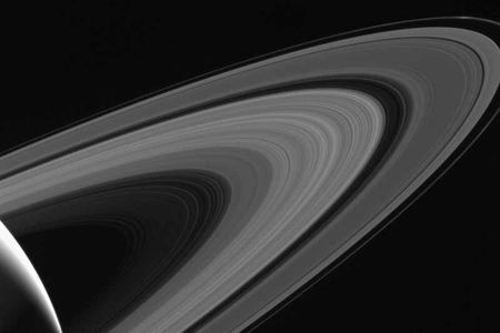 Behind Saturn's icy rings is the moon Tethys, illuminated by the planet's reflected sunlight.
