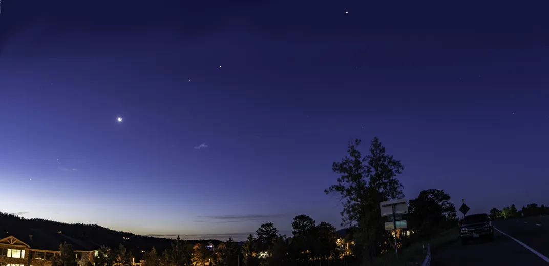 night sky view, captured from the ground, with several planets and the moon forming a line across the sky