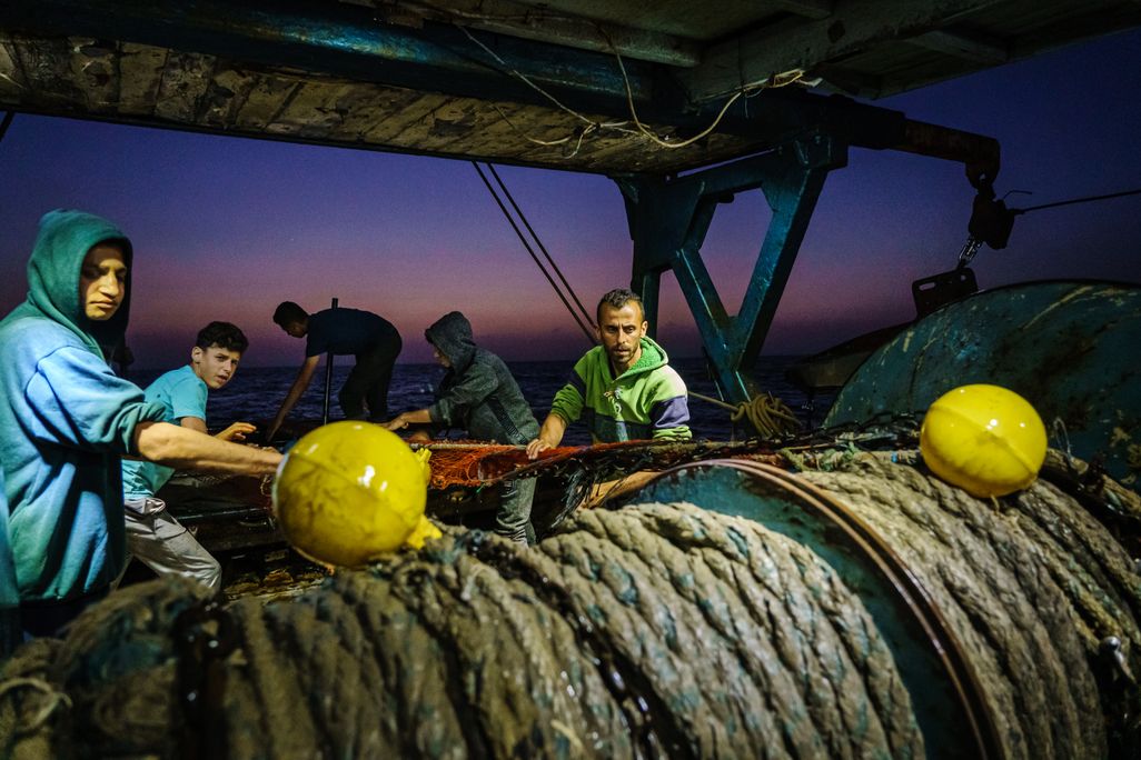 Fishers pull rope by hand at dusk on a fishing vessel in Gaza