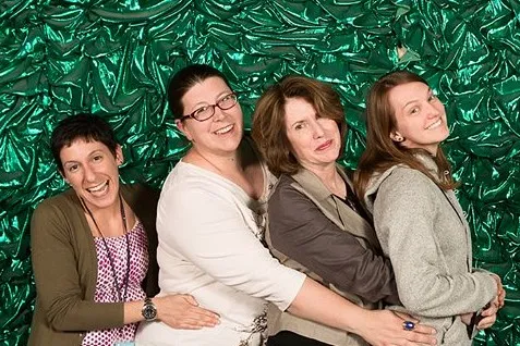 Four Caucasian women pose for a photo in front of a green backdrop