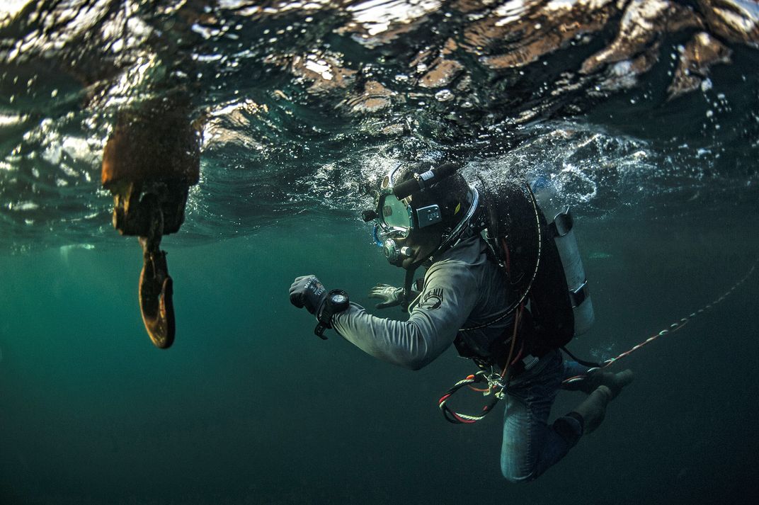 A diver with the expedition prepares to descend to the seafloor for excavations. Although the water at bottom is a balmy 83 degrees, divers must wear heavy suits to protect themselves from the jagged metal of the wreckage. Their helmets alone weigh more t
