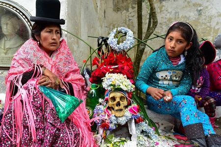 A woman in traditional Aymara dress sits with her daughter and their honored human skull, or ñatita, and a bag of coca leaves during the 2015 Fiesta de las Ñatitas in Bolivia.