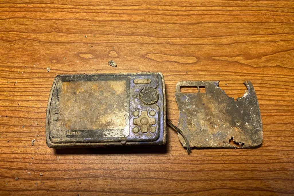 Mud-covered, broken digital camera on a wooden surface
