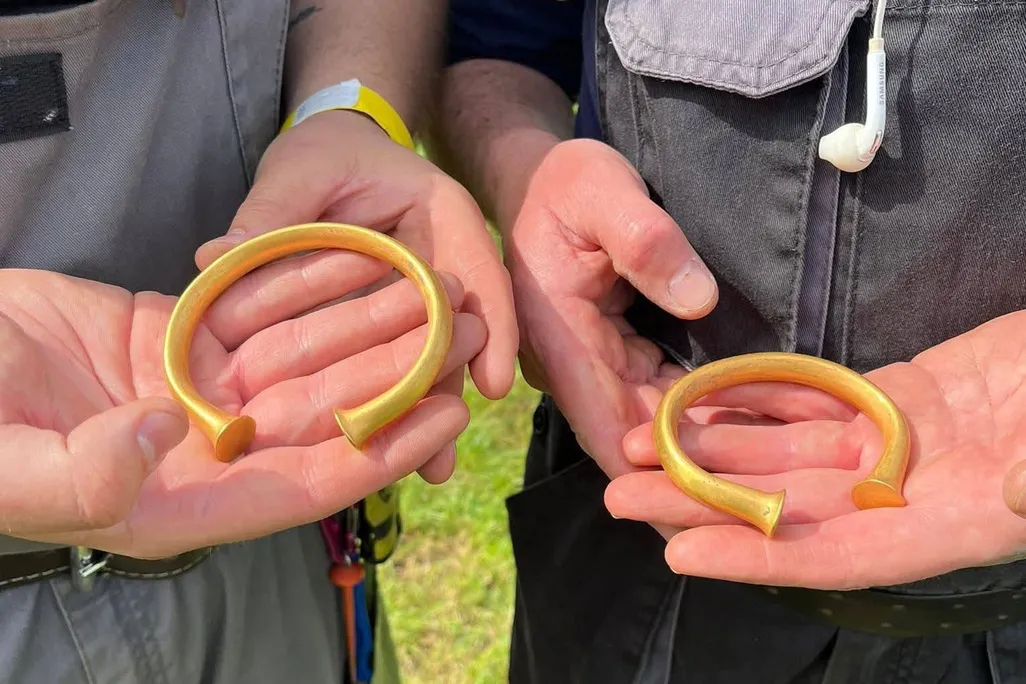 Two sets of hands holding gold armbands from the Bronze Age
