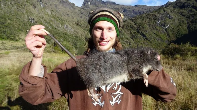 Man wearing a hat and holding up a large rat