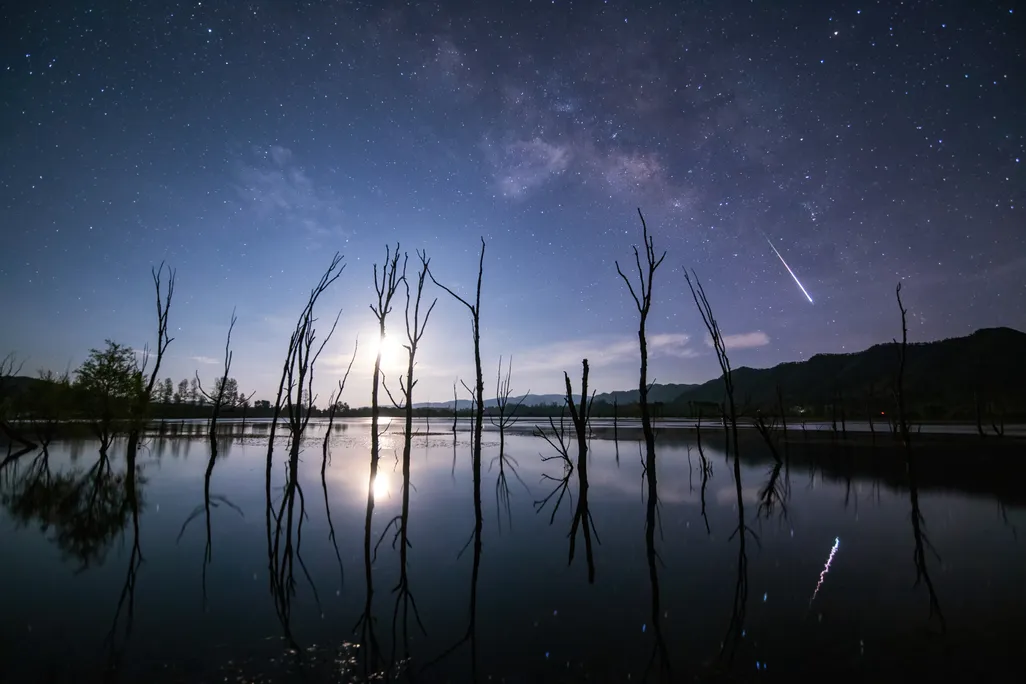 A shooting star and its reflection in a lake