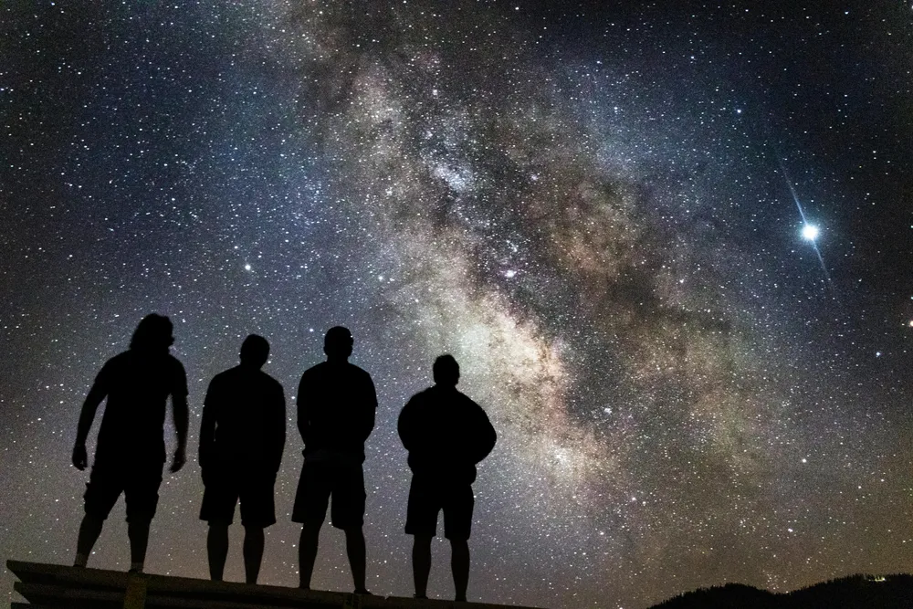 silhouettes of four people stand looking at the milky way