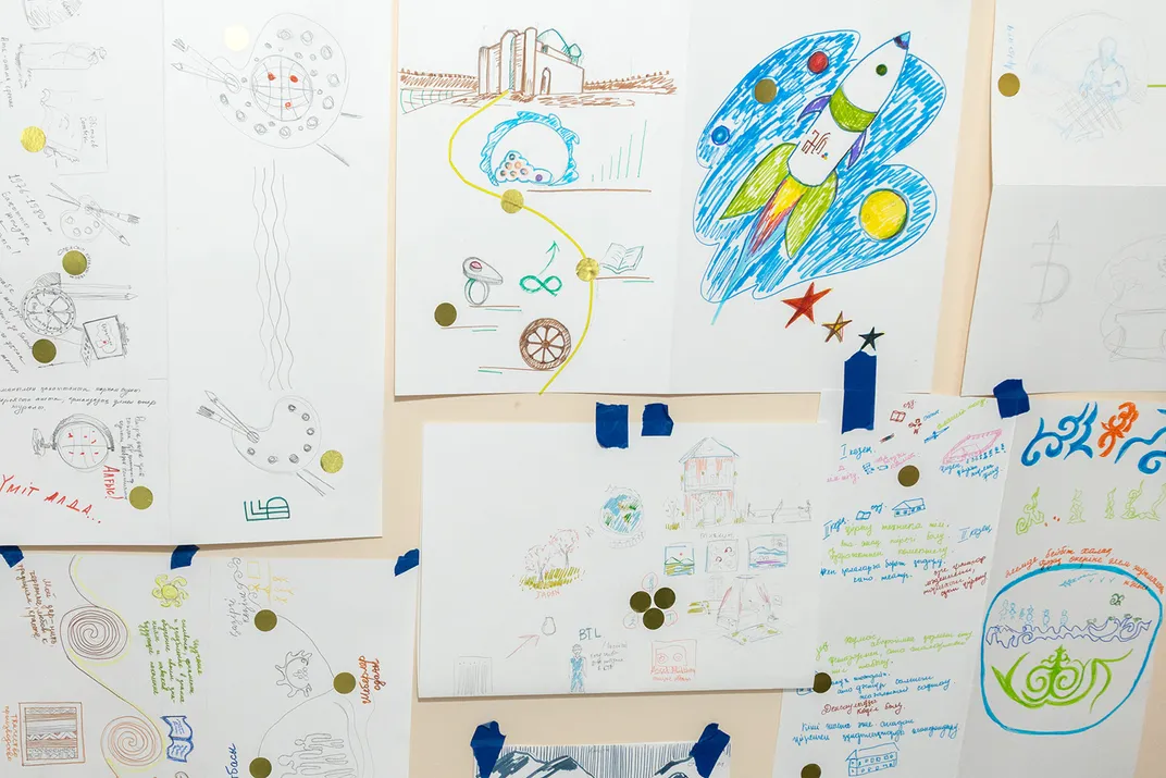 Several drawings taped up on a wall. One features a rocket ship flying through space. Others indicate a kind of pathway, from one item to the next.