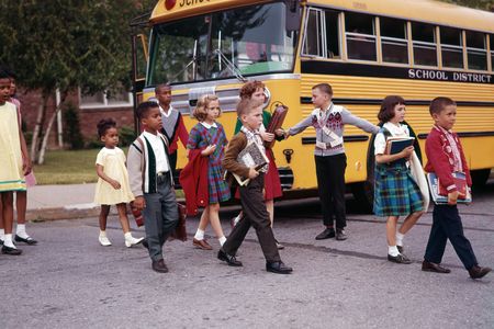 Children cross the street in front of a yellow school bus in 1965.