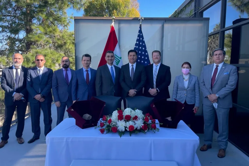 group of men and women in business attire standing outdoors in front of U.S and Iraq flags before two displays of stone tablet artifacts