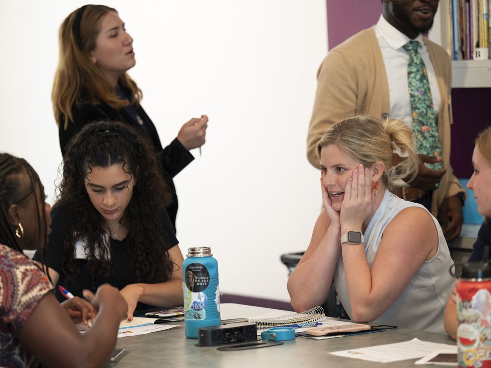 Teachers converse at a table, one woman with blond hair has her hands to her face