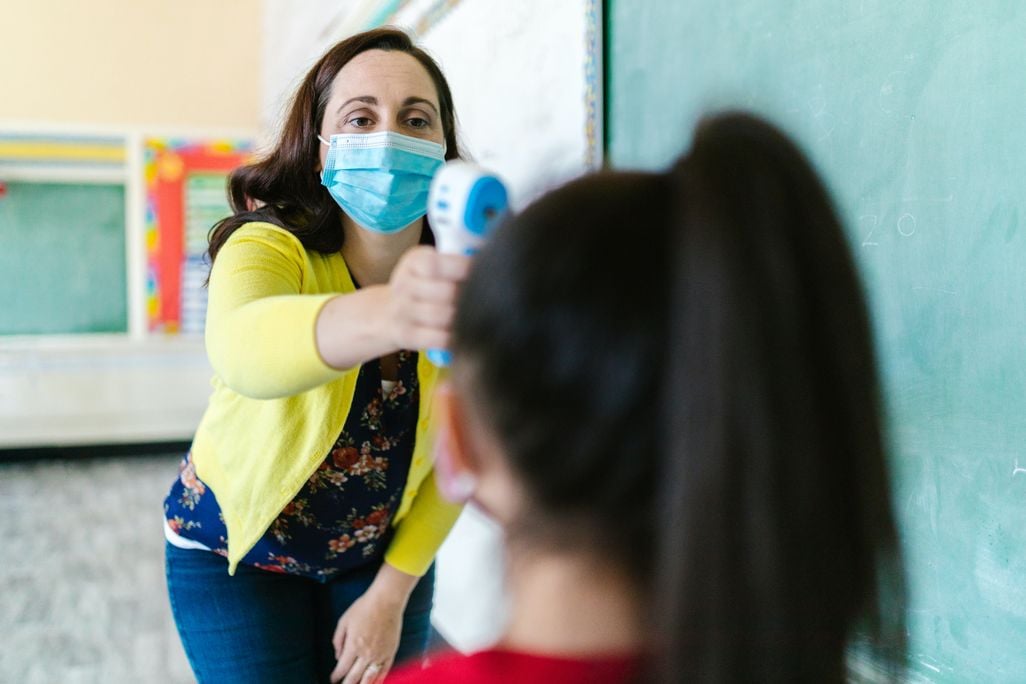 Woman wearing a mask taking a child's temperature