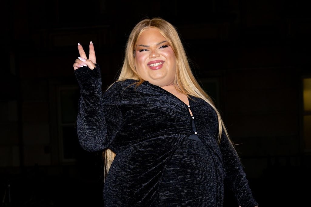 Woman with blond hair wearing black and holding up one hand with a peace sign